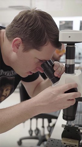 Michael Oshetski using microscope in a lab.