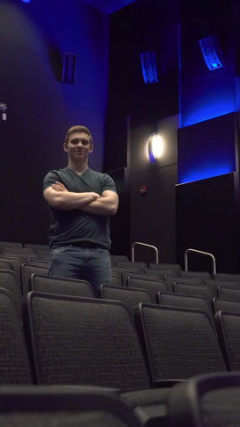 Andrew Sevigny standing with his arms crossed, inside a theater.