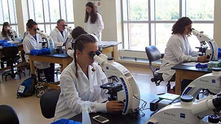 Students wearing lab coats, looking into microscopes.