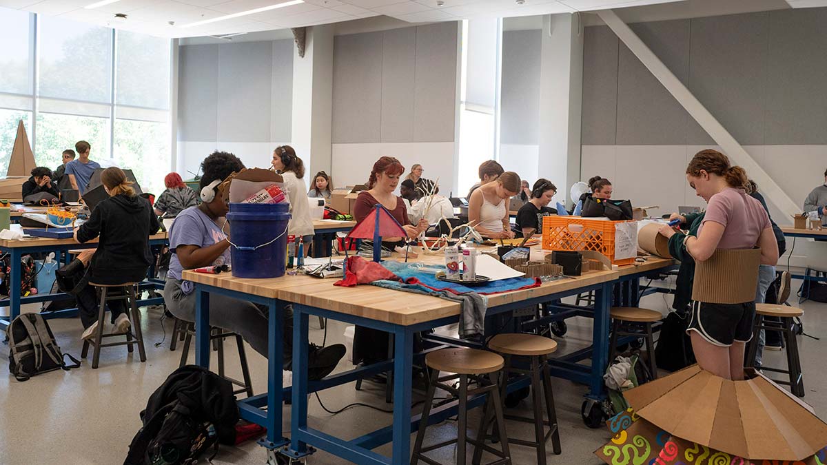 students build wearable cardboard pieces in a large workshop room.