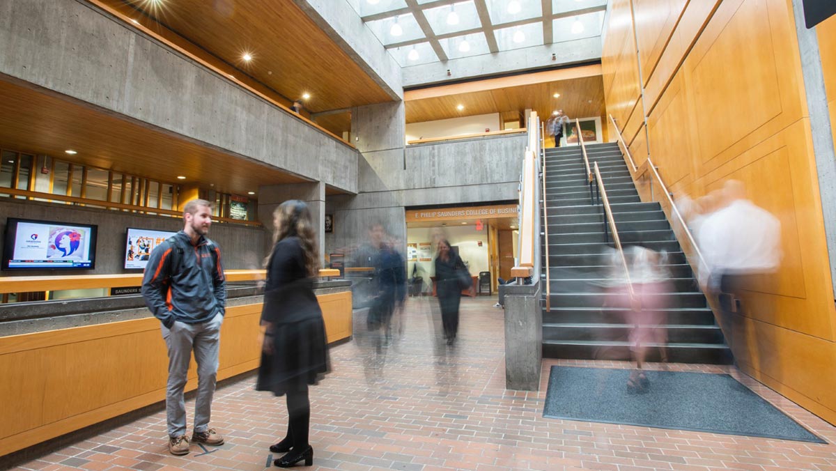 student and professor talk in an atrium as other people walk by, and their motion causes their images to be blurry.