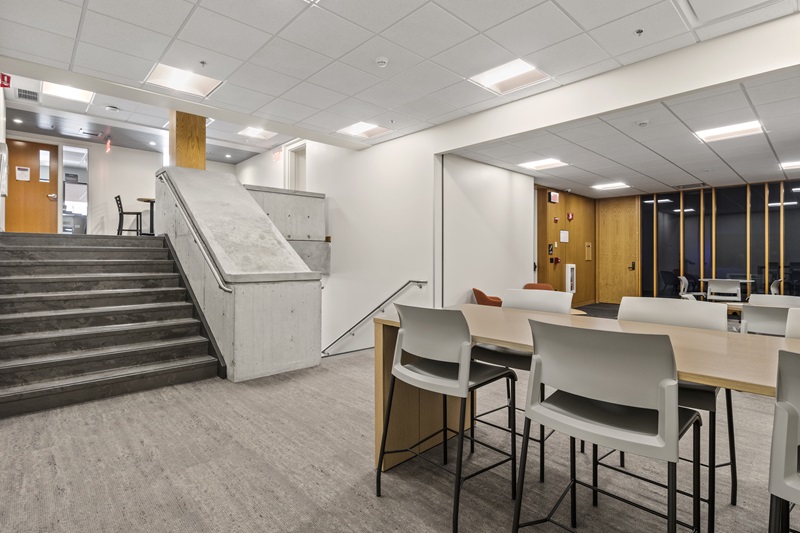 a common area with a set of stairs going up and another going down, with a table and chairs on the main level.