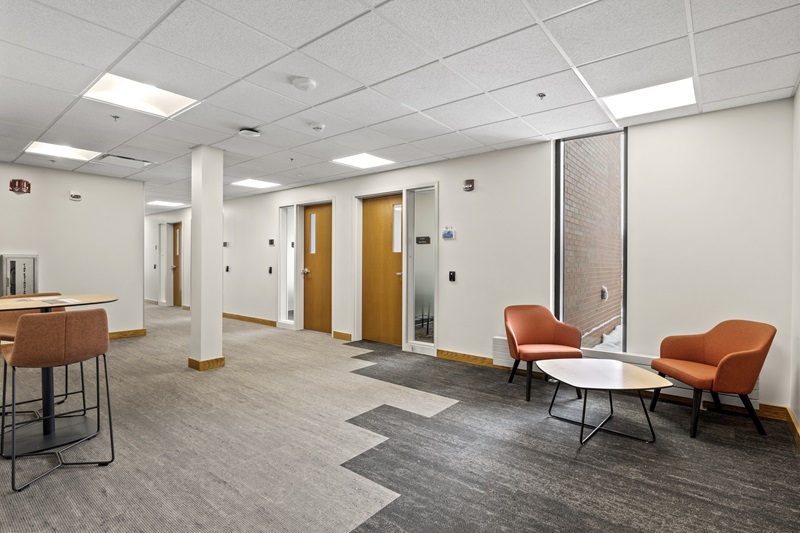 a common area with tables and chairs that leads to a hallway with offices.