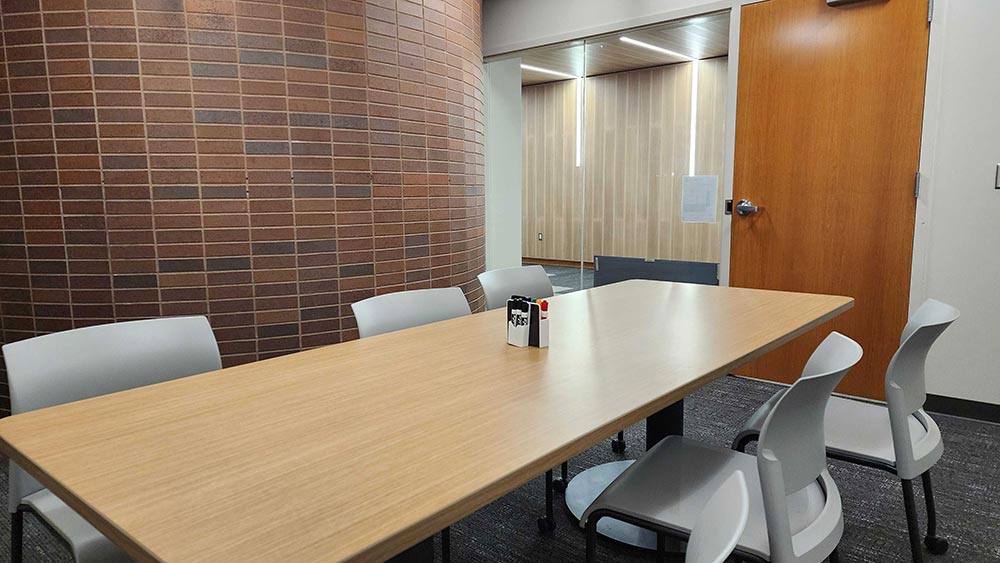 a meeting room with a table and six chairs, and a brick wall.