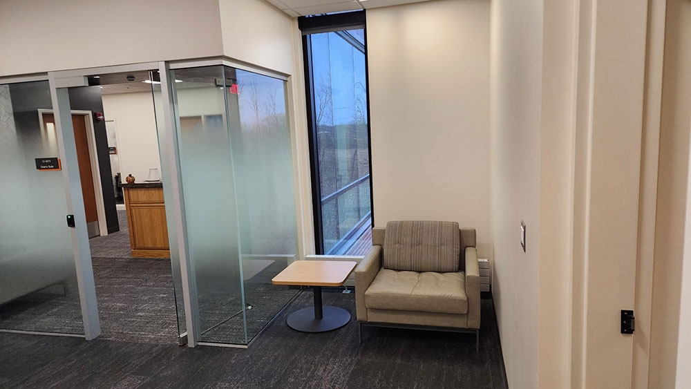 a corner next to a glass office, with a chair and end table.