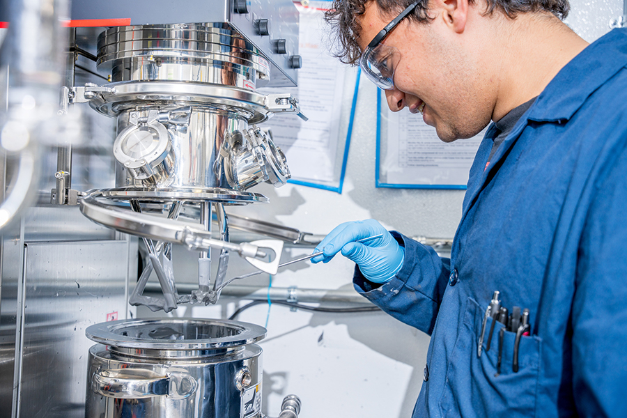 A student wearing a blue lab coat and working with a machine in the RIT Battery Development Center