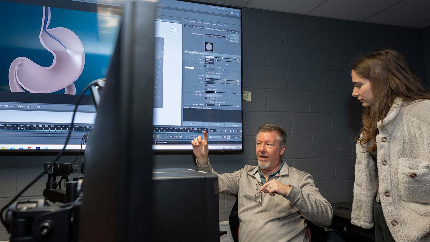 professor talks to a student in a lab with a large screen showing a digital image of a stomach.