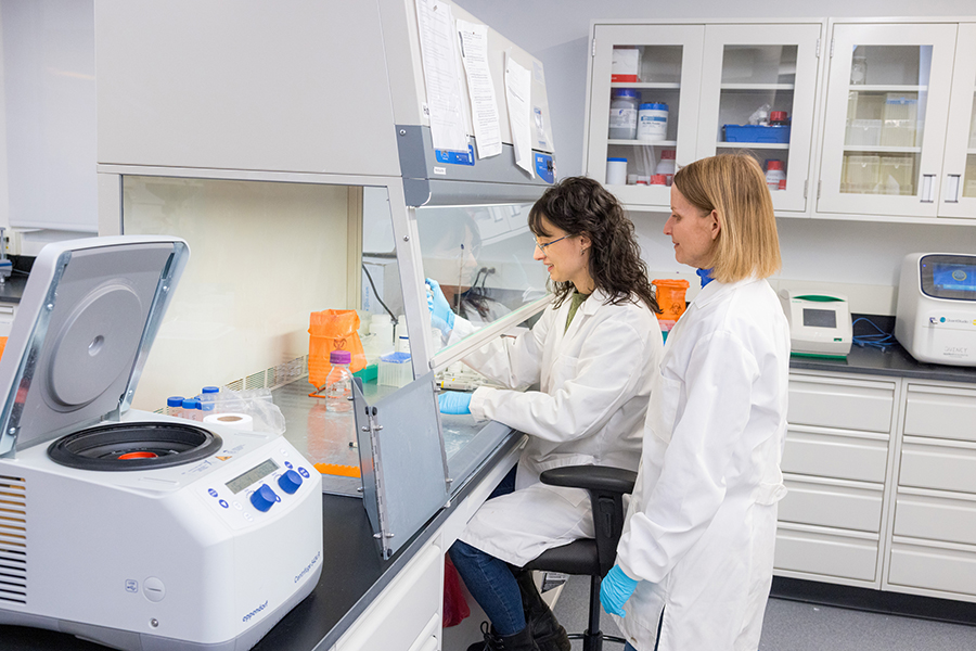 A professor standing behind a student and observing them working in the Nano Bio Lab at RIT.