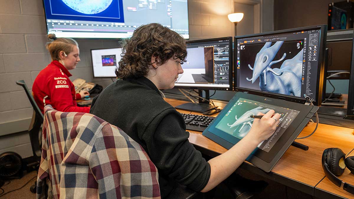 a student draws on a tablet, which also displays on a computer screen.