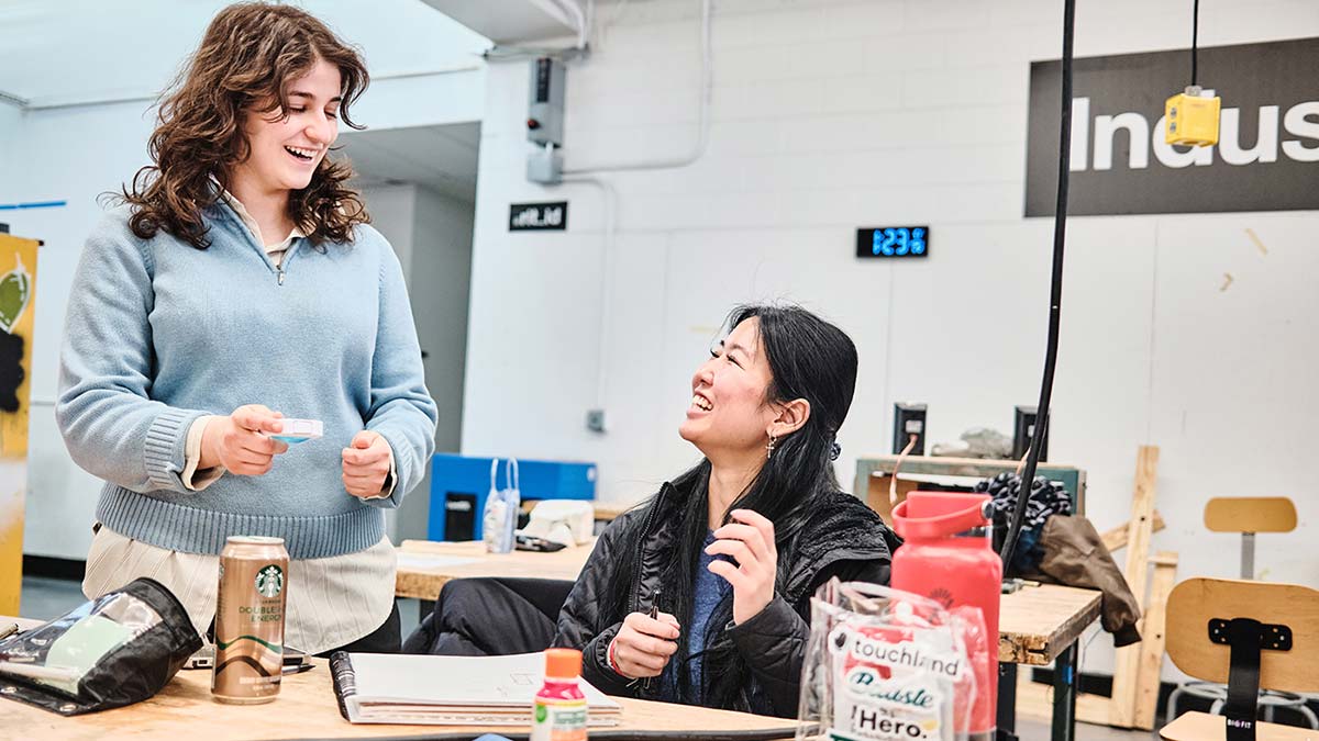 Two smiling students at a work station in the industrial design studio.