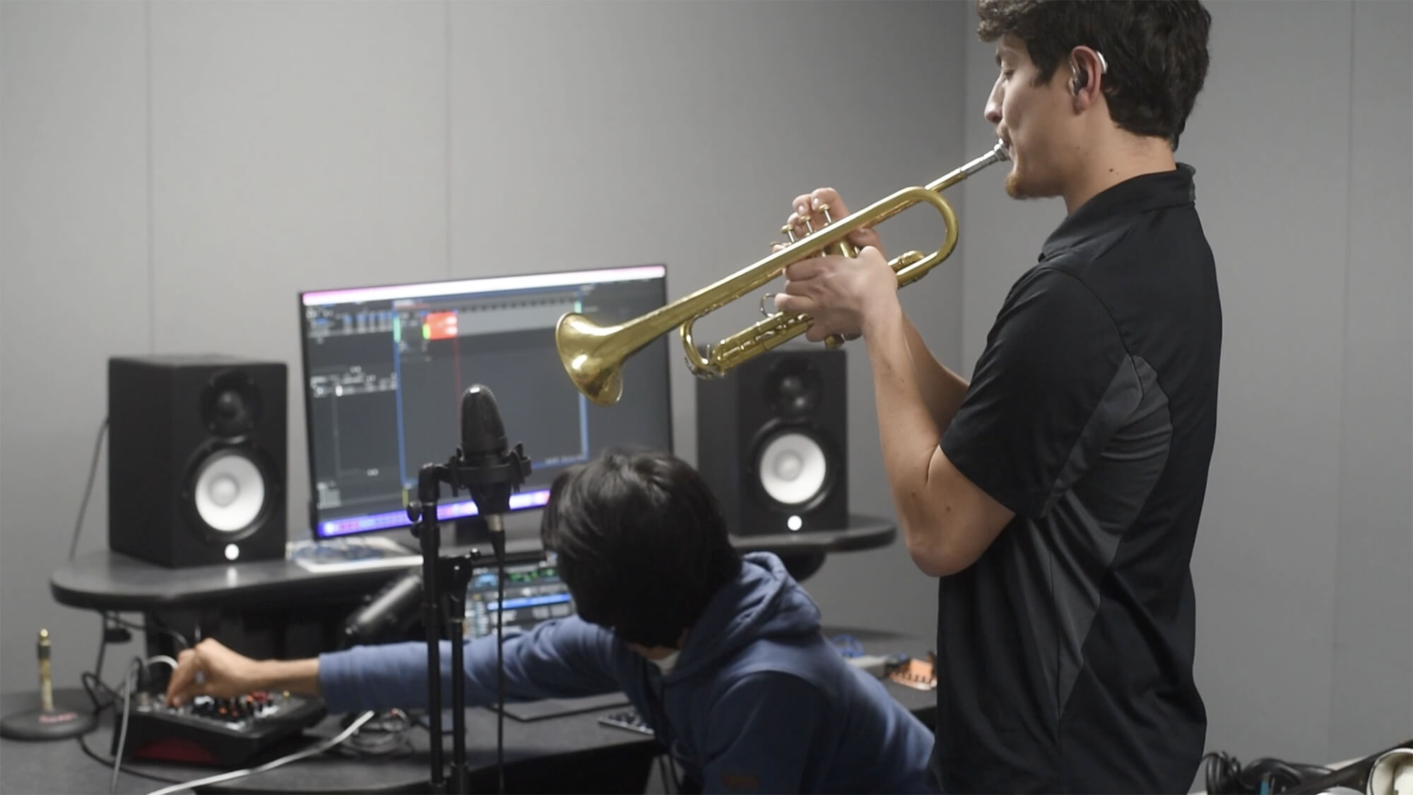 Daniel Sarch plays the trumpet as a fellow student edits on a computer.