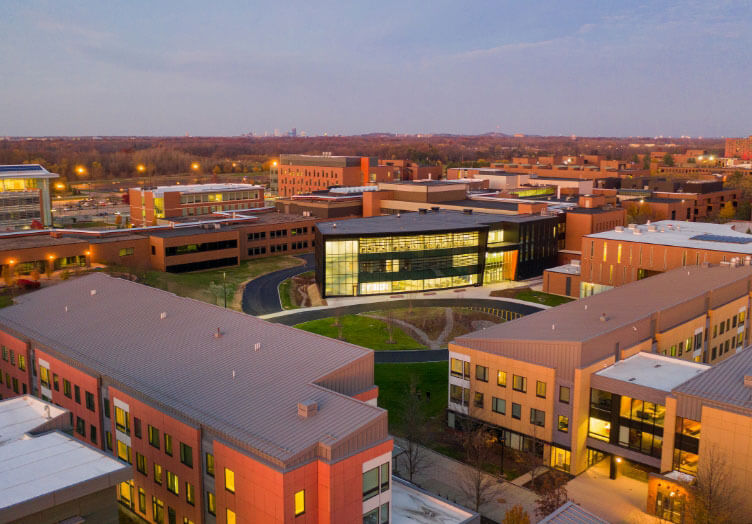 drone shot of the ESL Global Cybersecurity Institute, a black building with lit up windows surrounded by brick buildings on RIT campus.