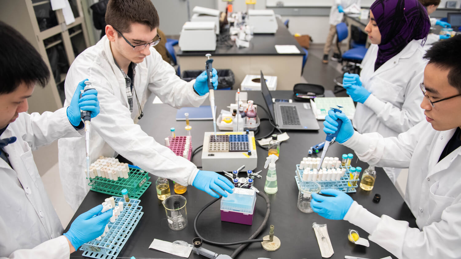 students in a lab setting wear lab coats use pipettes.