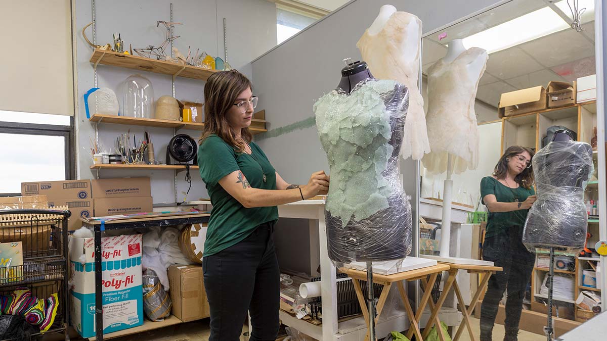 student adjusts a light green fabric on a mannequin.