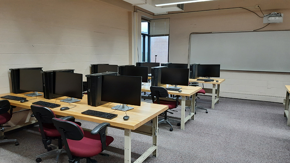 A computer lab with rows of tables with computers and chairs.