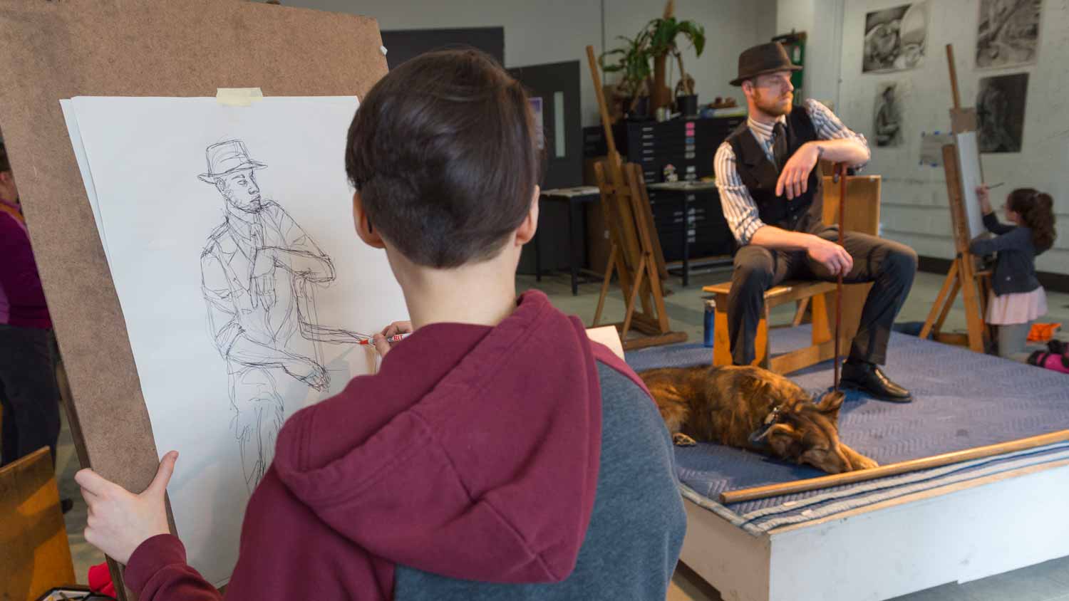 A model with a hat on posing for a student drawing him
