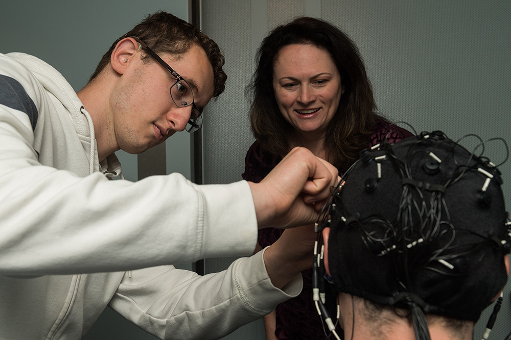 student researcher adjusts a cap with electrodes on a subject.