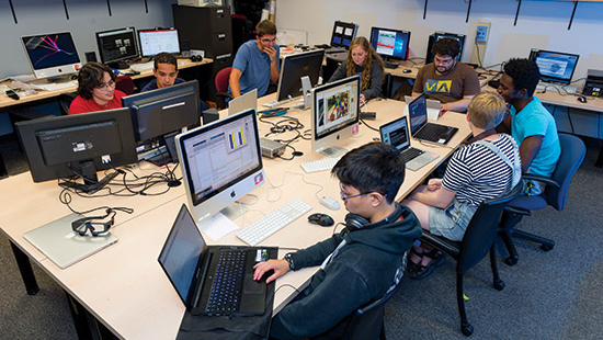Students sitting around a desk, using computers.