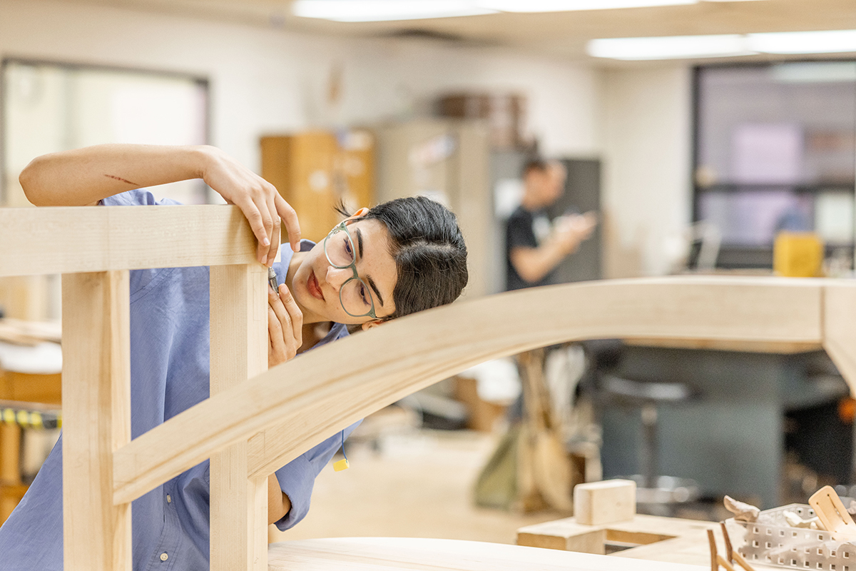 An RIT student uses a hand tool on a furniture piece.