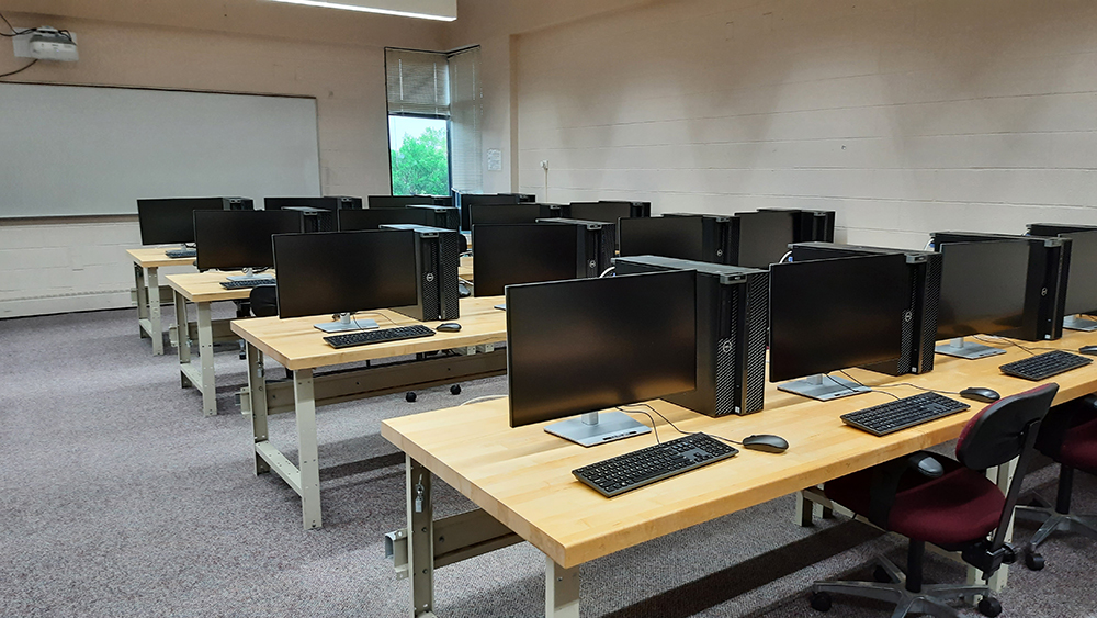 A computer lab with rows of tables with computers and chairs.