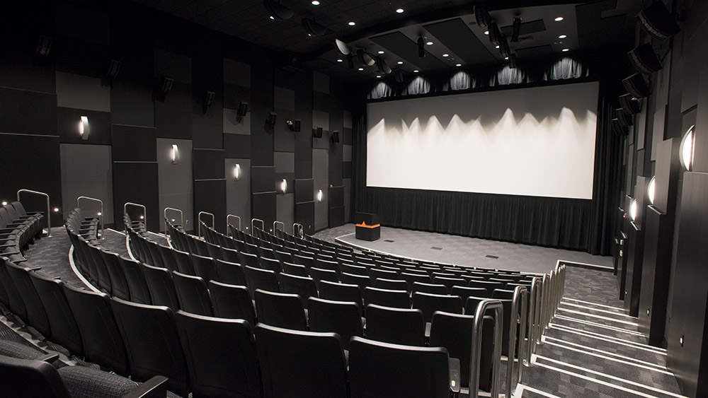 empty theater with stadium seating, stage, podium, and large screen.