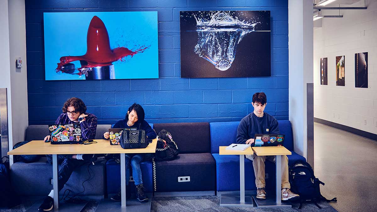 students work on laptops in a lounge area.