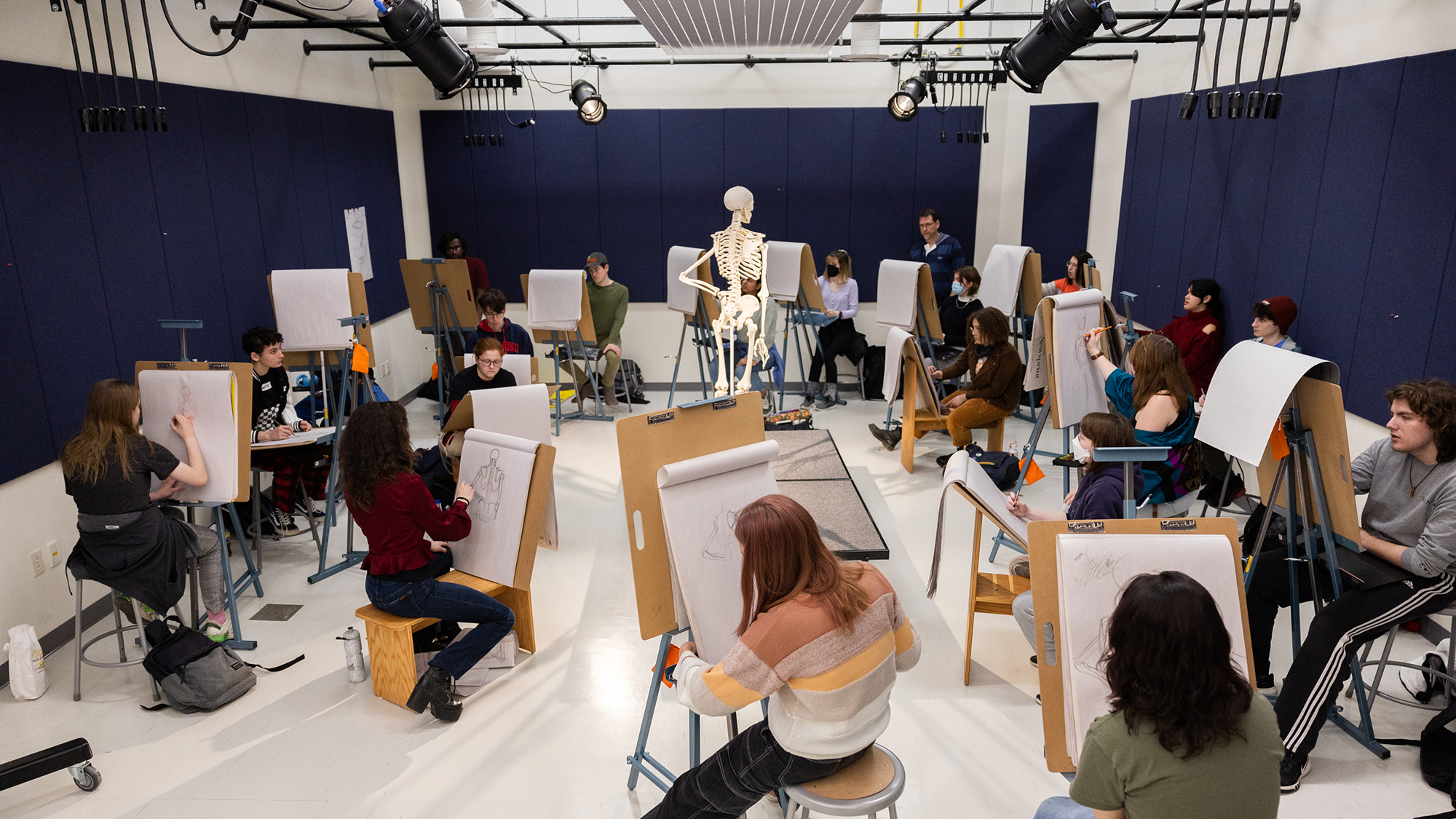 Students draw in a studio with a skeleton model in the middle of the room.