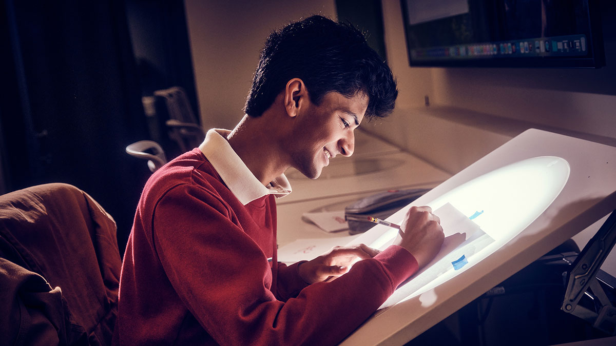 A smiling student draws on a light table.
