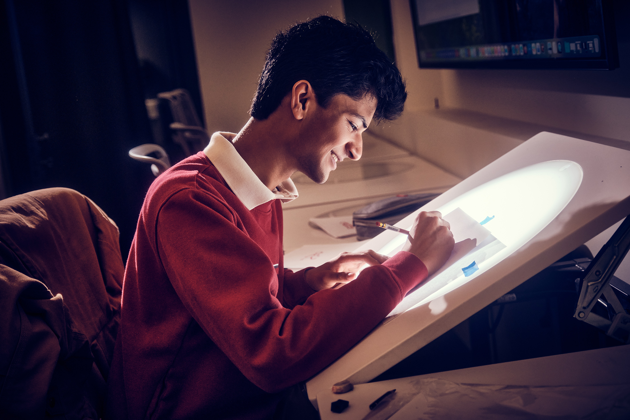 A smiling student draws on a light table.