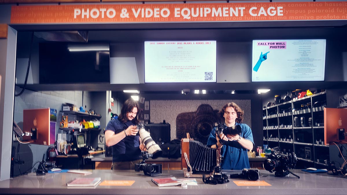 Two Cage employees behind the counter of the Cage, looking at camera equipment.