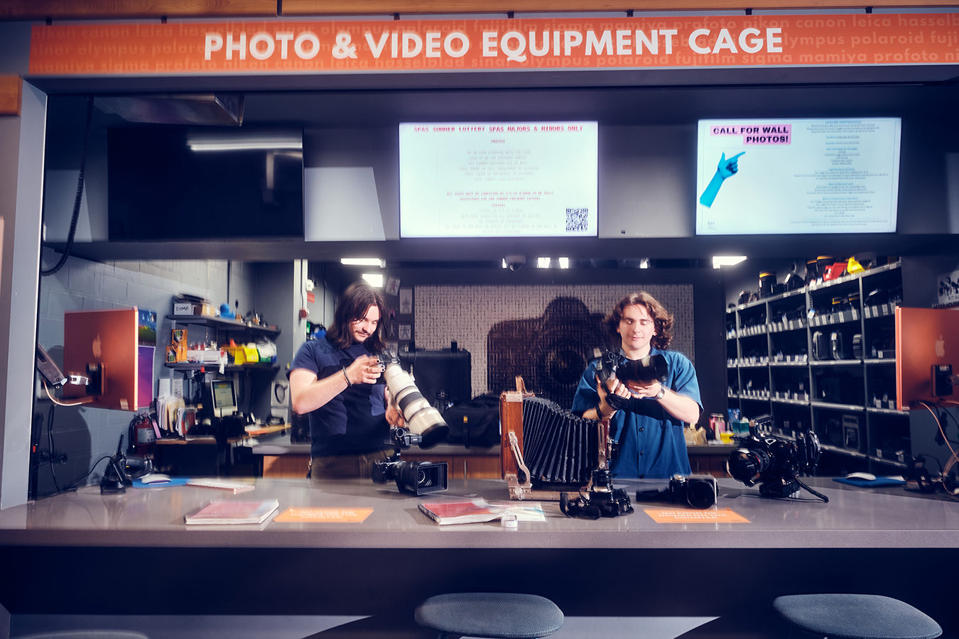 Two Cage employees behind the counter of the Cage, looking at camera equipment.
