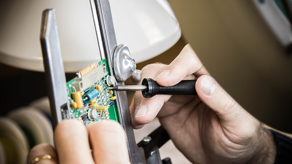 Electronic circuit board being repaired with tool.