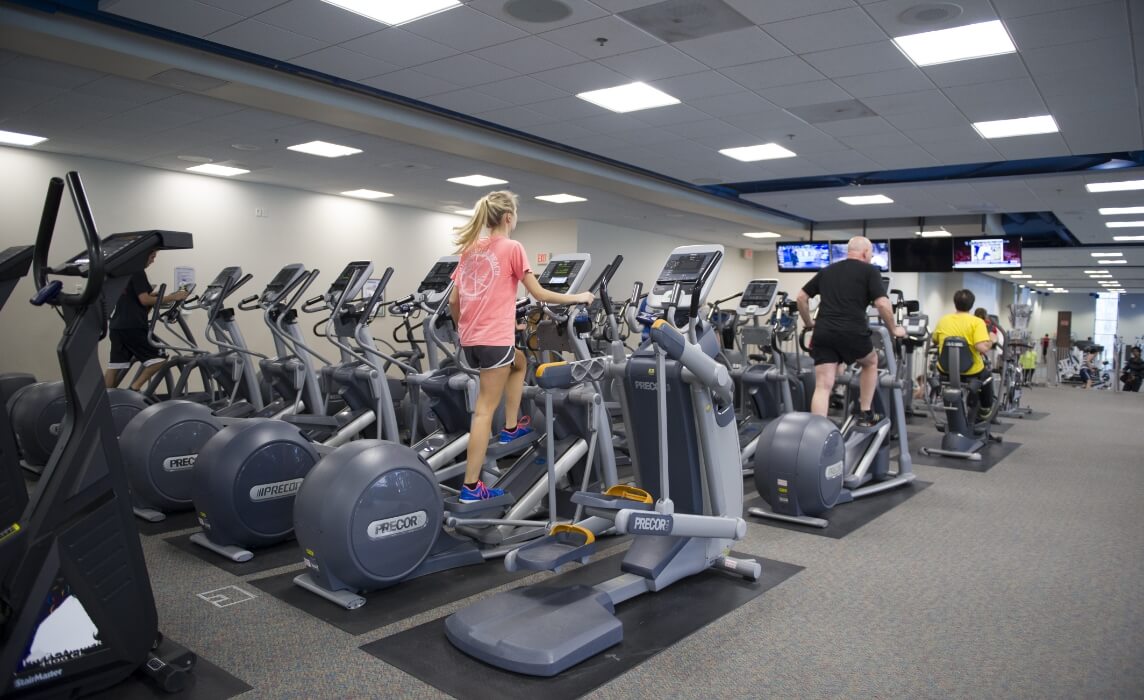 Two rows of ellipticals in the Wiedman Fitness Center with people using the exercise machines