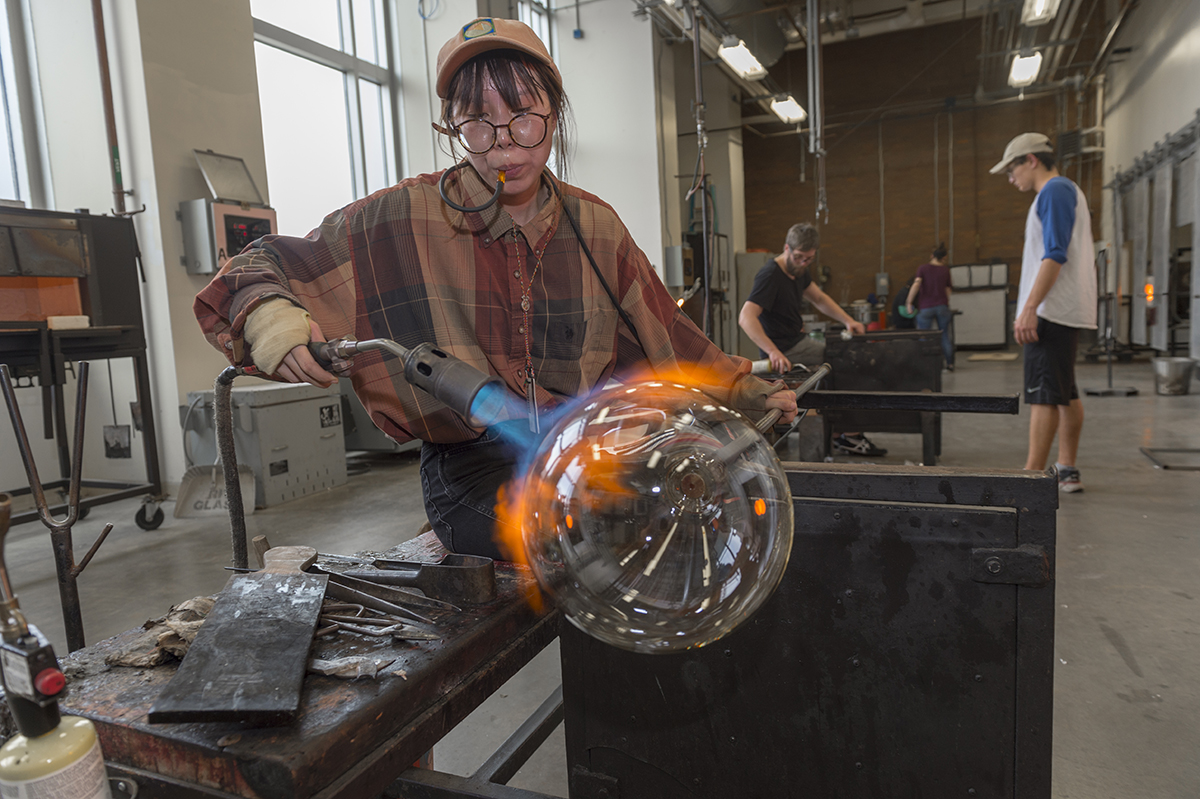 A student lights a torch to a glass object.