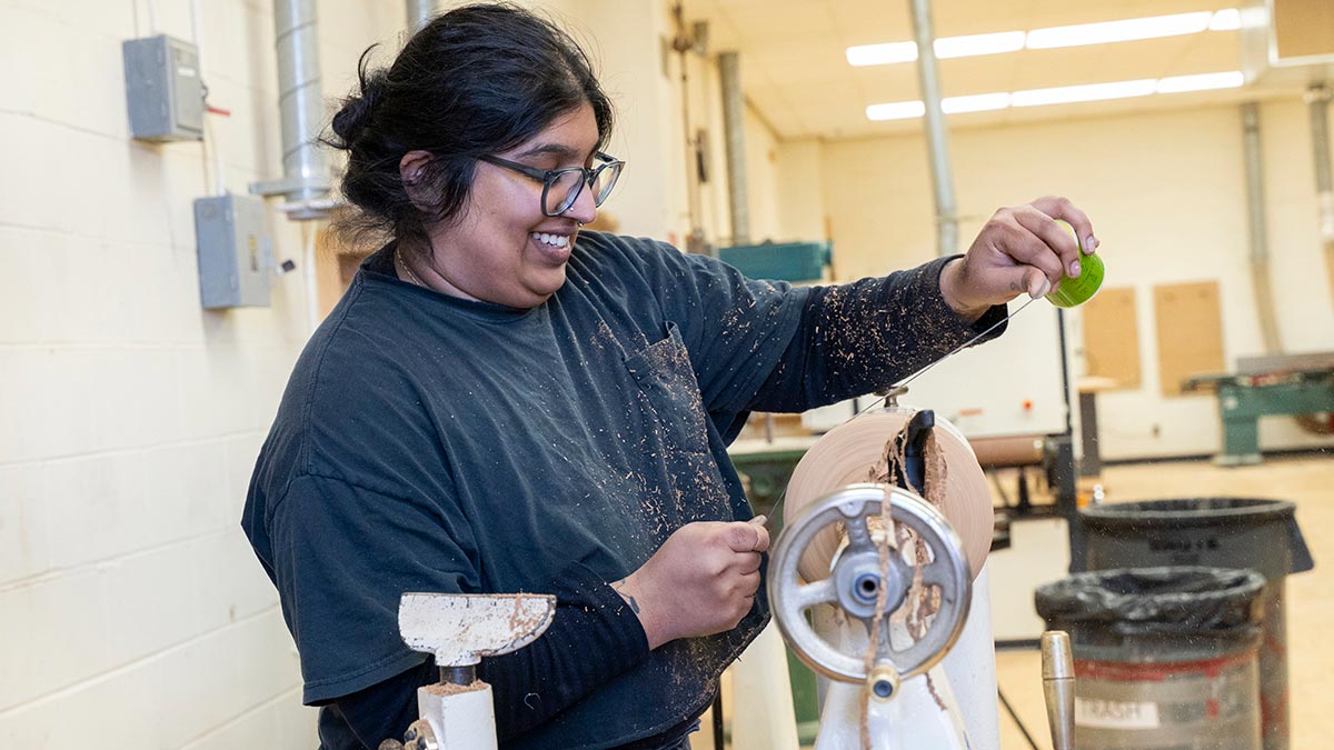 student smiles as she uses a lathe.