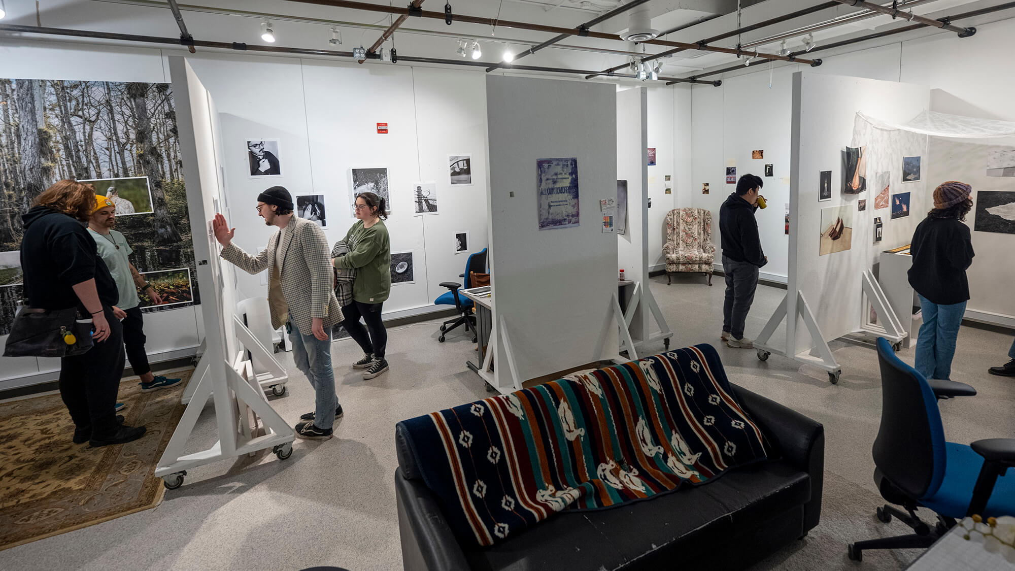 people walk through an art gallery space, with white walls and rolling dividers.