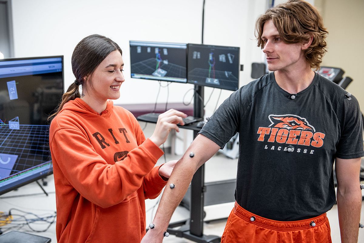 A female student placing sensors on a male students arm, waist, and neck.