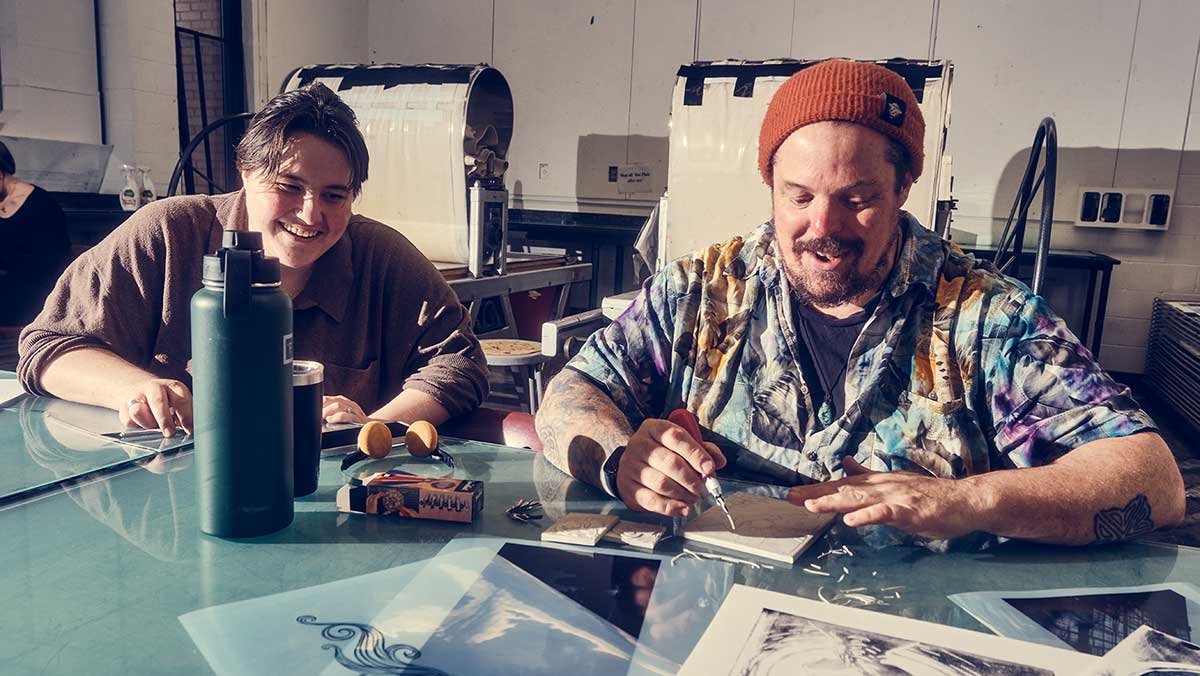 Two smiling students work in the printmaking studio side by side.