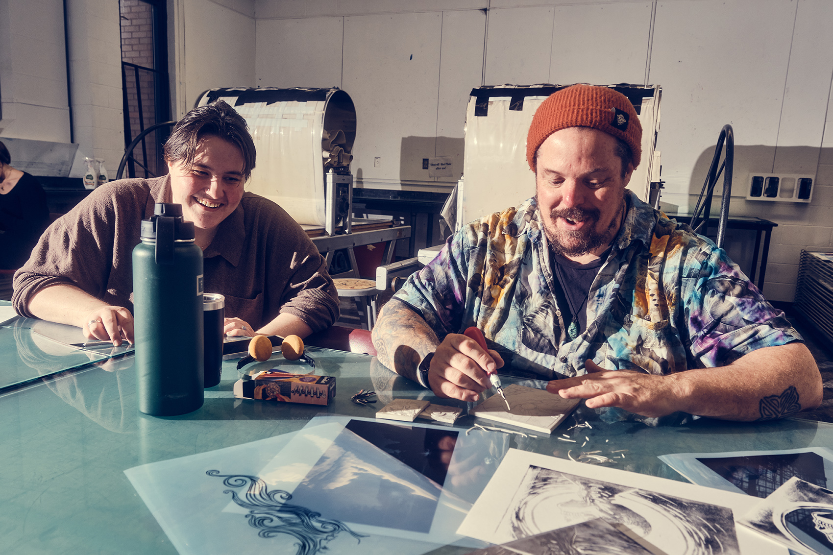 Two smiling students work in the printmaking studio side by side.