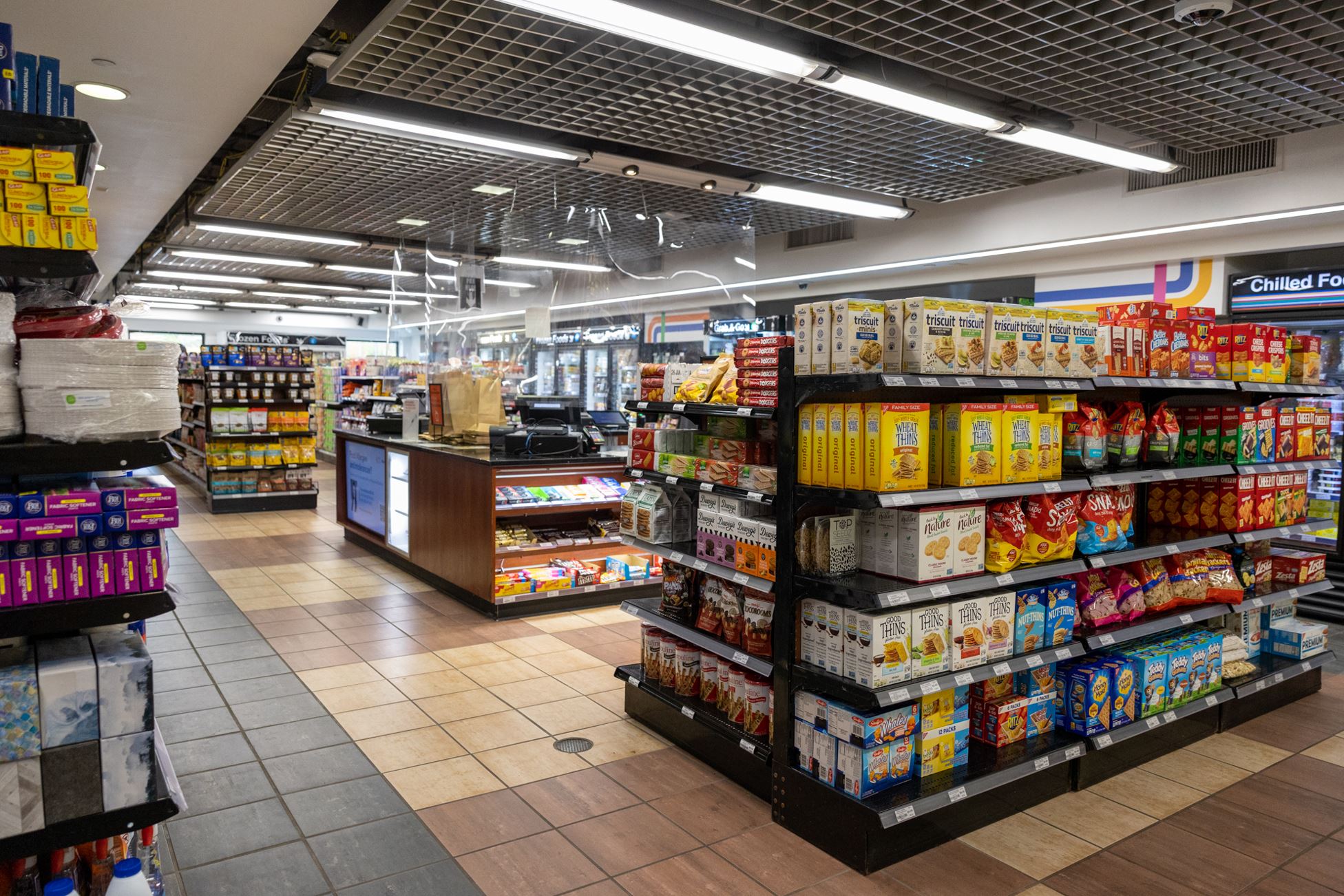 Shelves stocked with snacks, toiletries, paper products, and cash register in the center