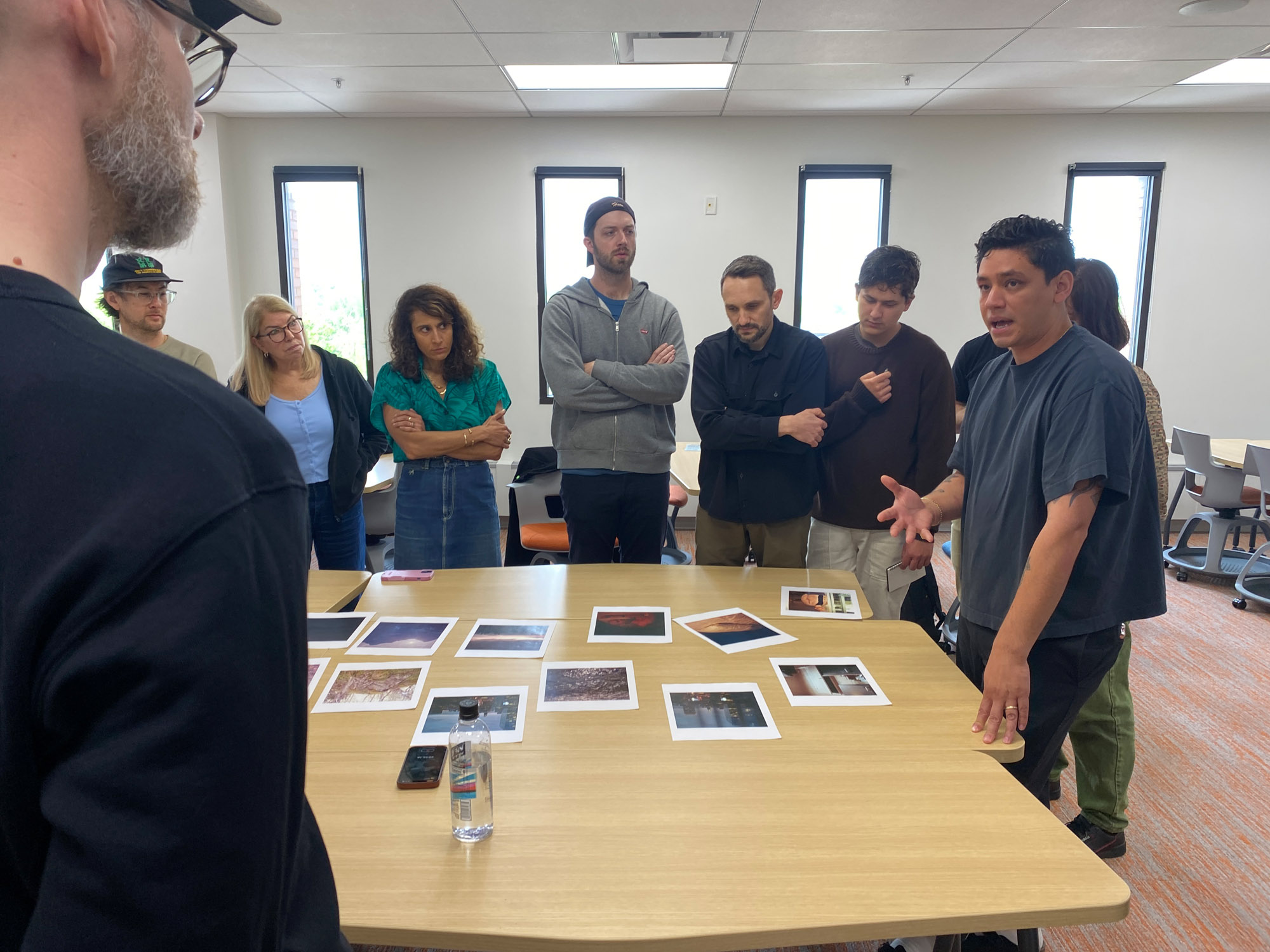 A group of people sit around a table looking at photo prints.