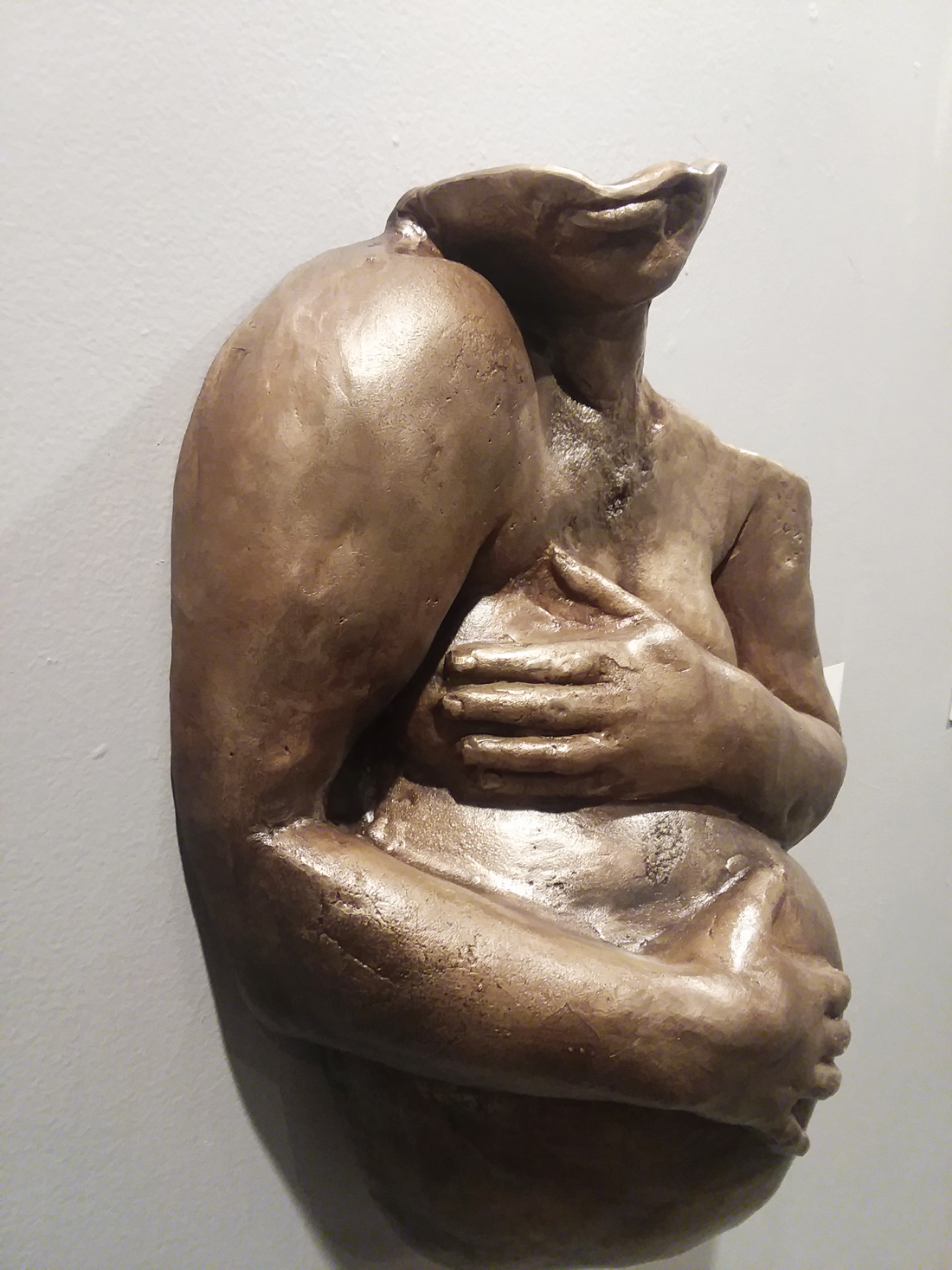 A bronze sculpture of a person holding their chest and stomach.