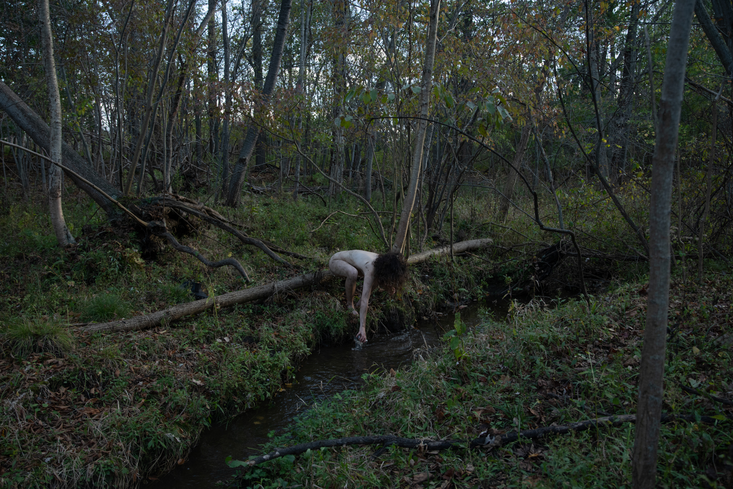 A woman straddles a fallen tree limb in a forest.
