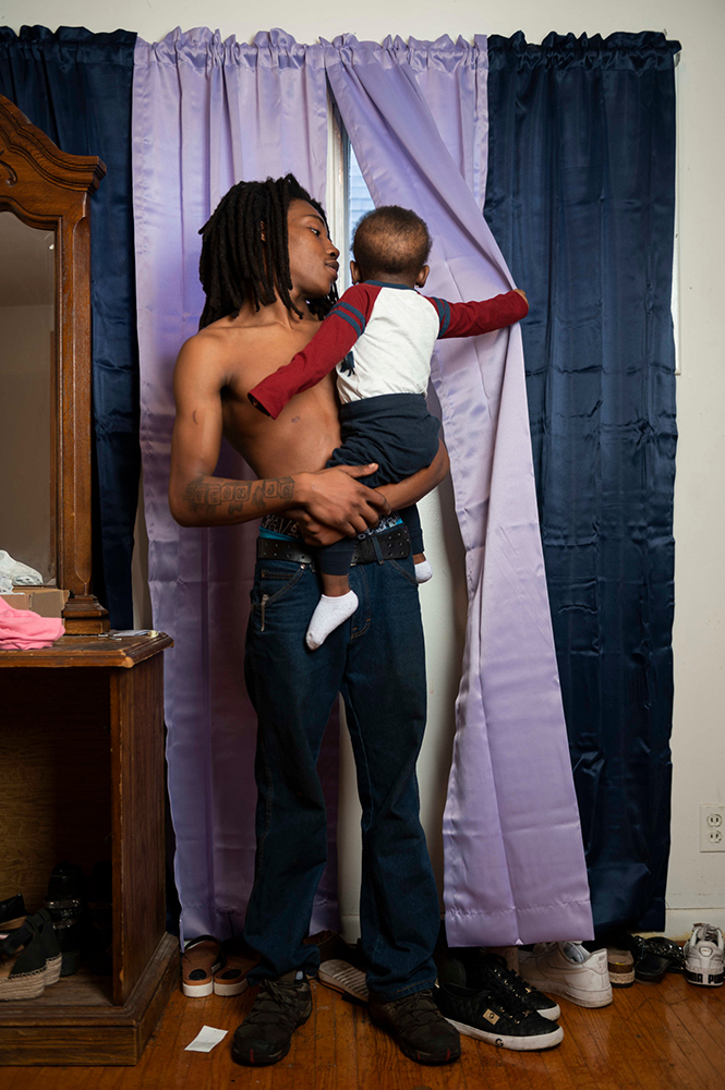 a young adult holding a baby while looking out a window.
