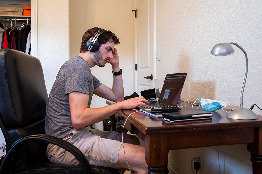 student sitting at desk at home wearing headphones and working on laptop.