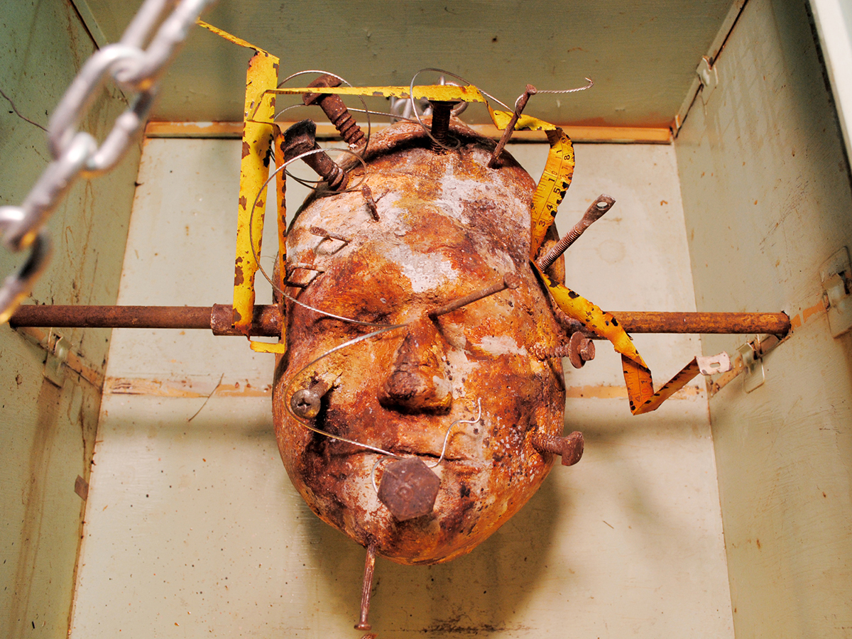 A found object sculpture of a head with rusty nails and bars going through it.