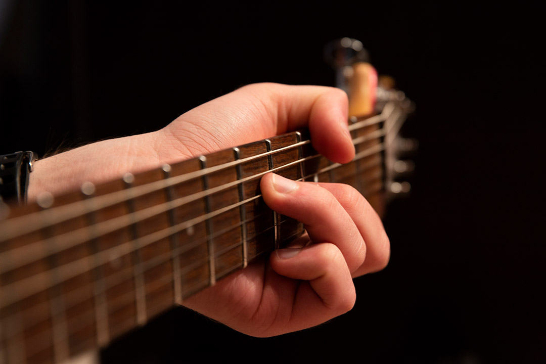 closeup of hand on fretboard of a guitar.