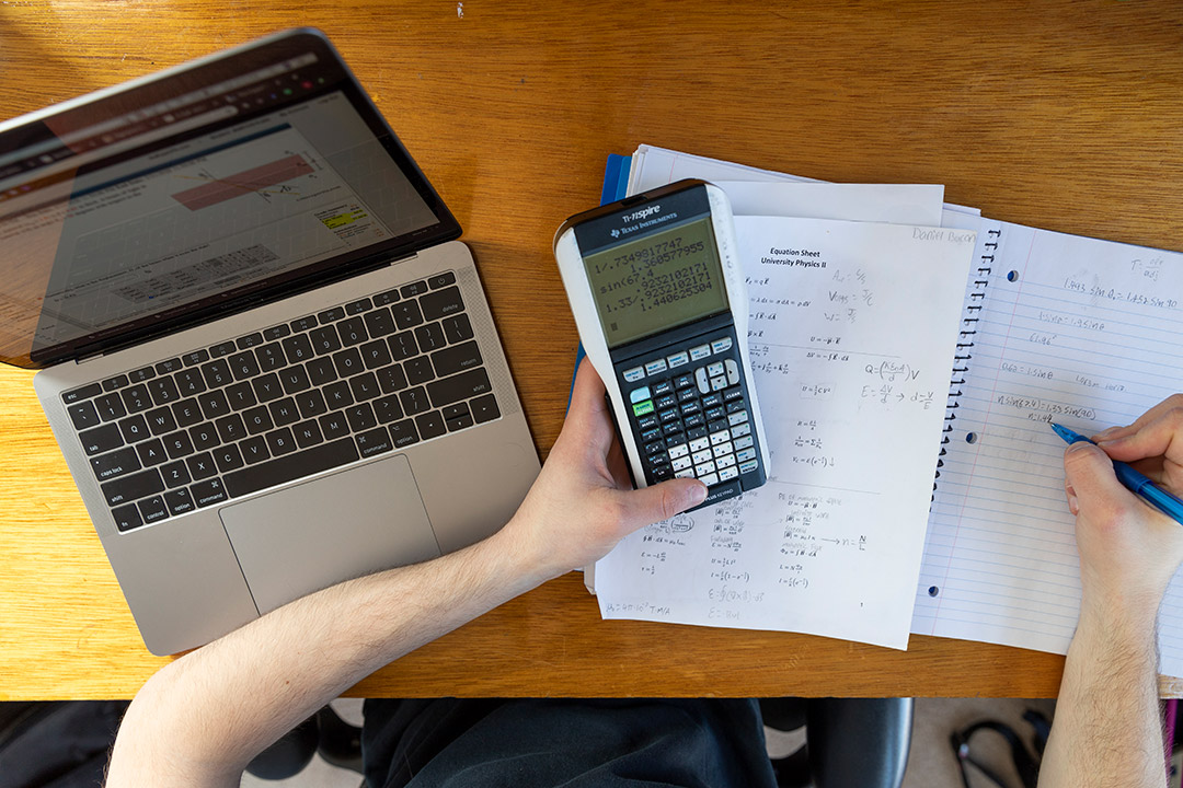 overhead view of student working on laptop and graphic calculator.