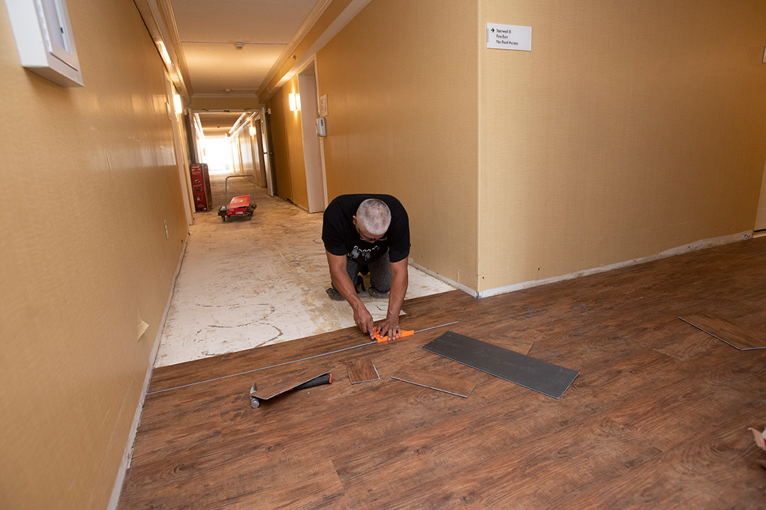 person installing vinyl flooring that looks like hardwood in a former hotel.