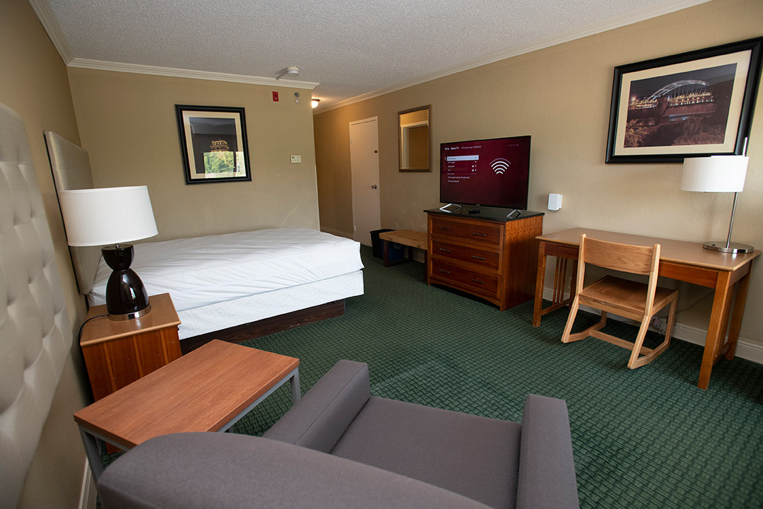 hotel room with a bed, chair, desk, and TV.